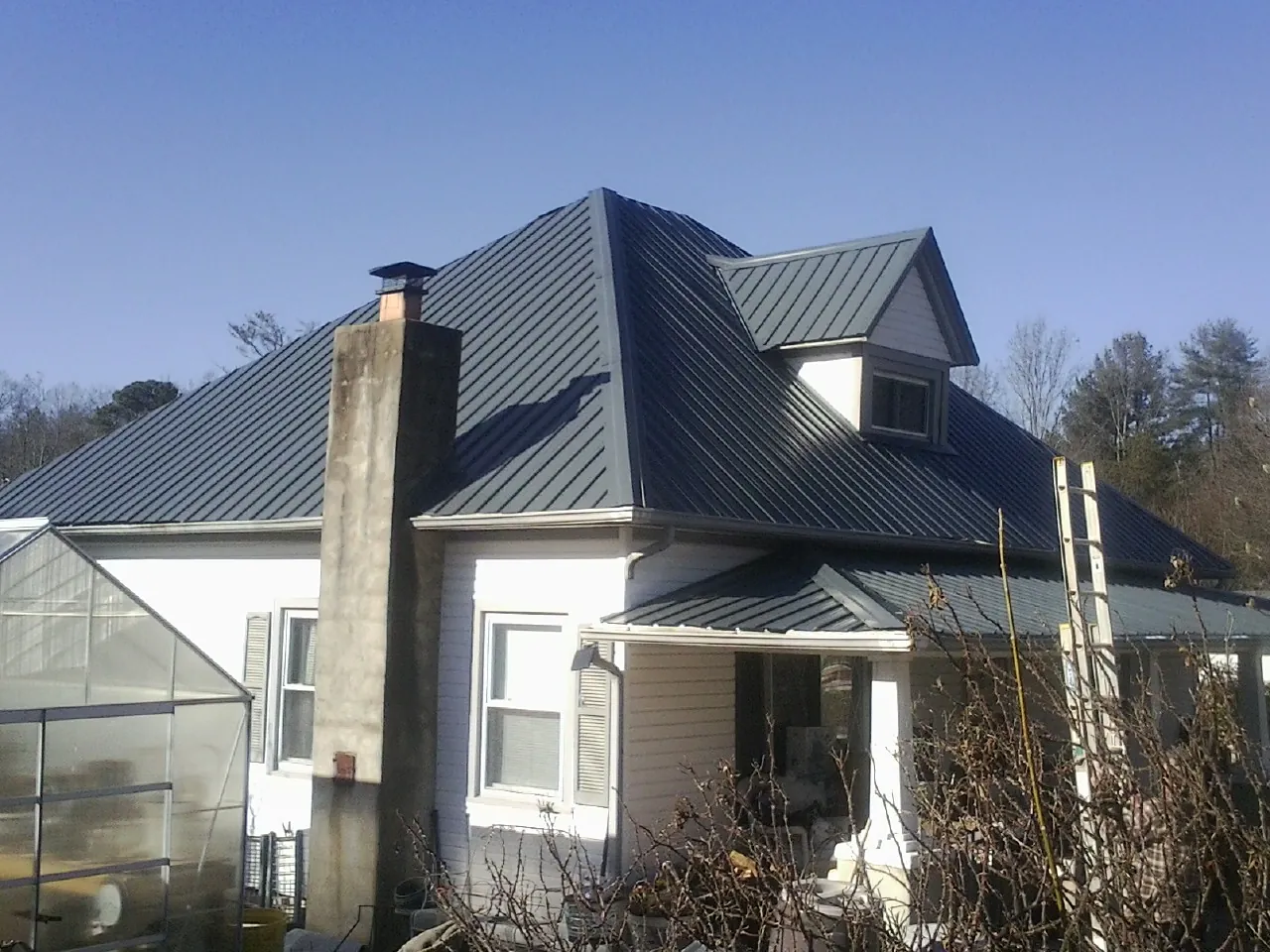 Dark blue standing seam metal roof on a white farmhouse with dormer — Slate & Tile Roof Repair by Roofing Brothers in Juda