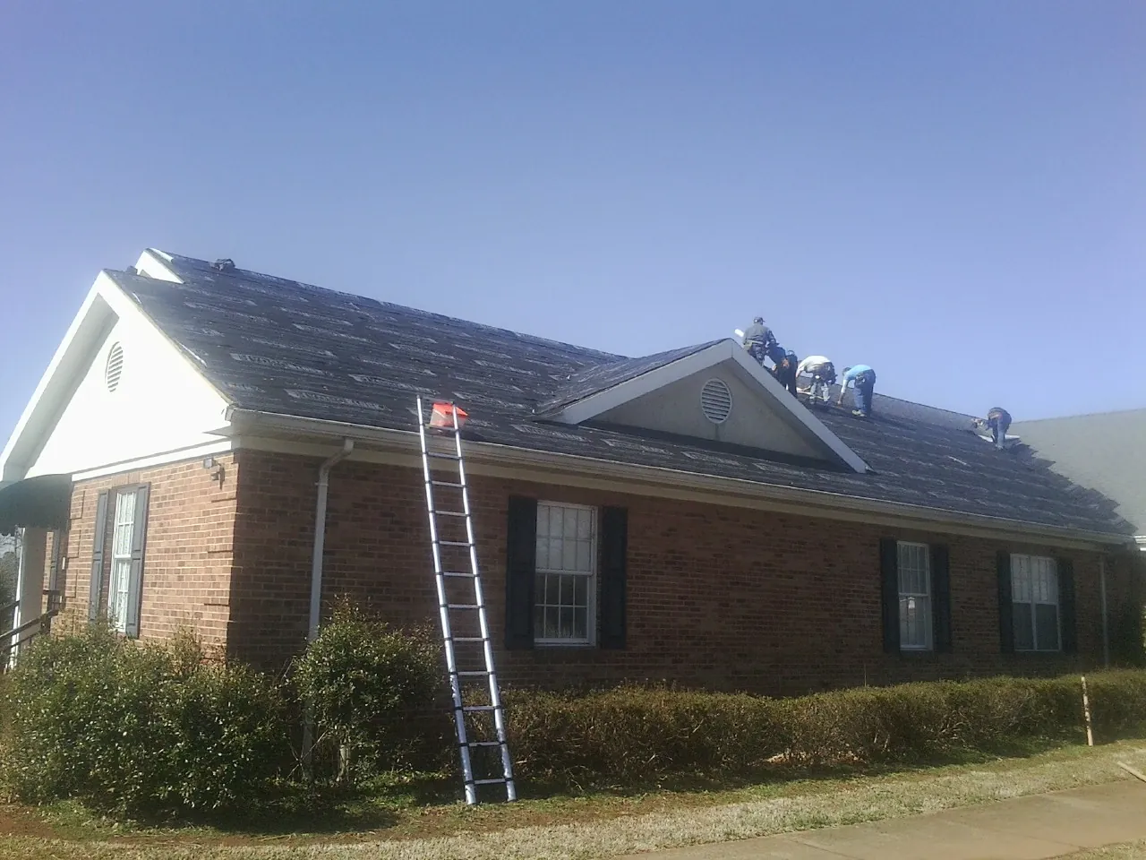 Crew tearing shingles off a brick ranch roof with a ladder set — Emergency Roof Repair work by our crew in Juda