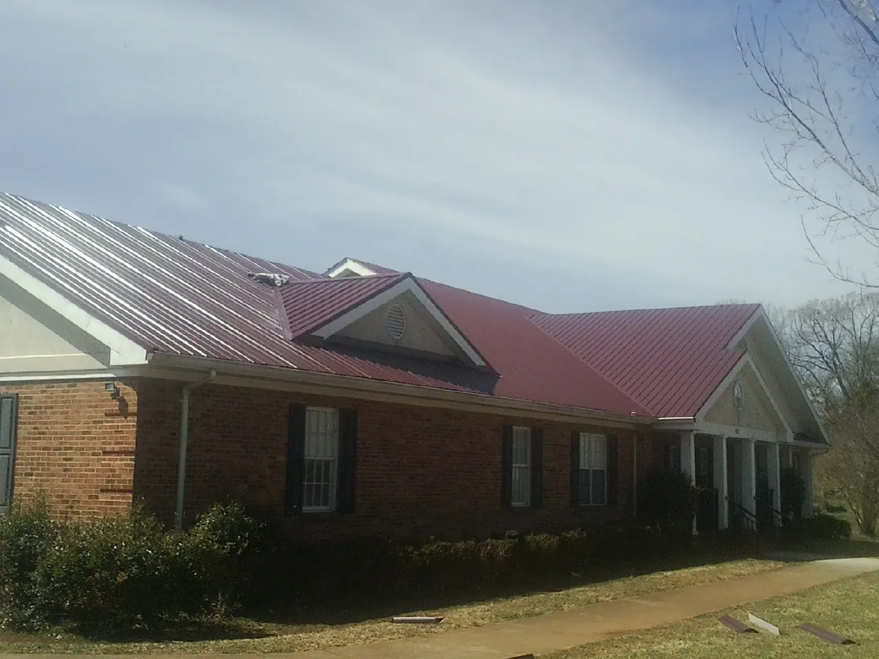 Red metal roof with gabled entries on a long brick building, from a Hail Damage Roof Repair job in Juda