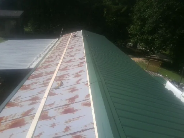 Old rusted panels beside newly installed green metal roofing — Wind Damage Roof Repair by Roofing Brothers in Juda
