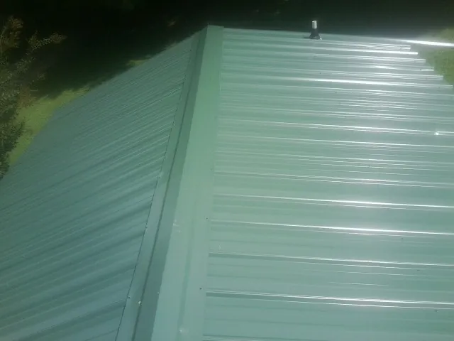 New green metal panels meeting at the ridge of a roof — Flat Roof Repair work by our crew in Juda