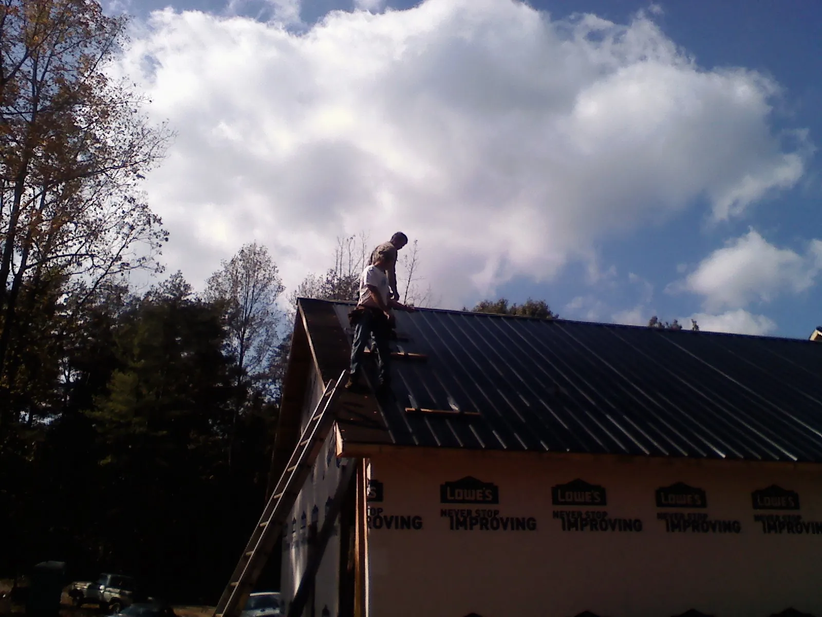 Roofer fastening dark metal panels high against a cloudy sky, from a Roof Inspection job in Juda