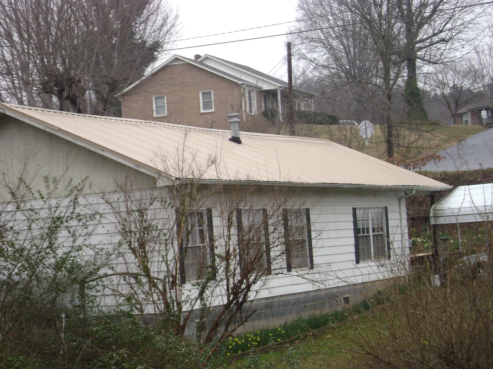 Tan metal roof on a white sided house set into a hillside — Commercial Roofing by Roofing Brothers in Juda
